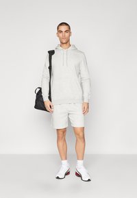Sudadera gris clara y pantalones cortos a juego, hechos de una tela suave, combinados con zapatillas blancas. Una bolsa de deporte negra está colgada del hombro.