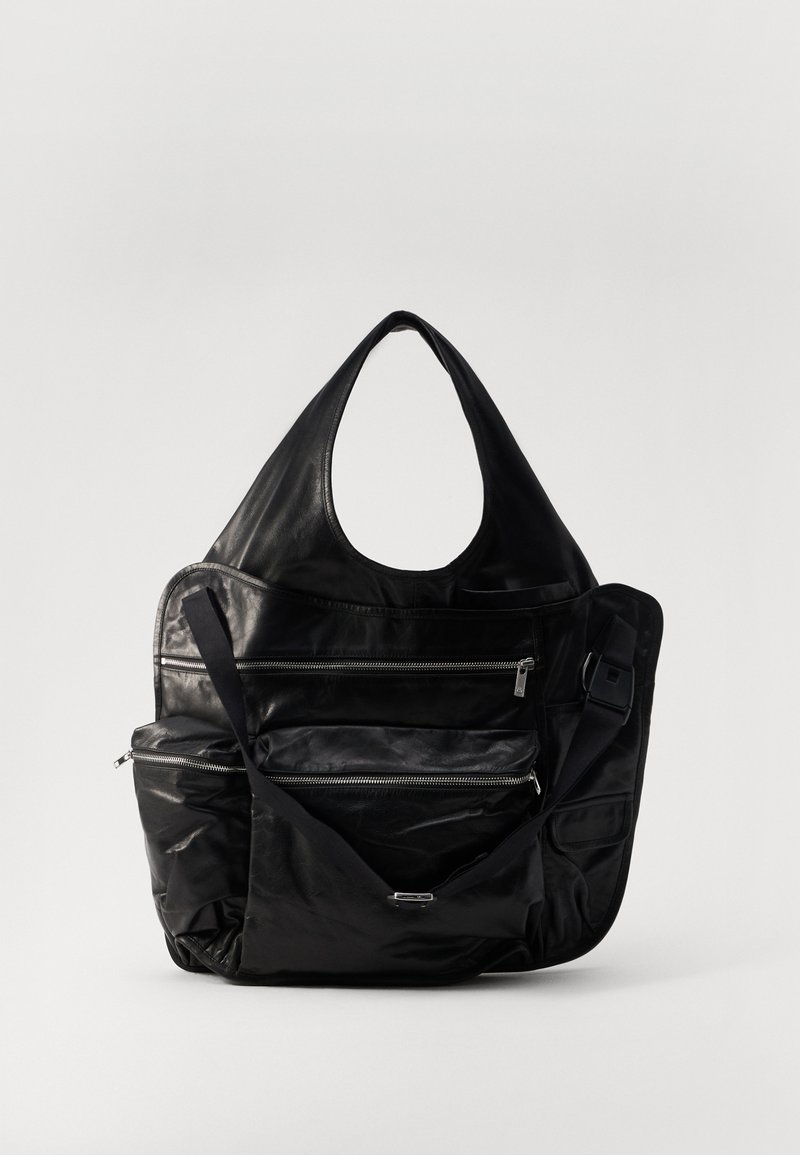 Sort lædertaske med stor hobo-form, der har flere lynlåslommer og en justerbar skulderrem. Glat tekstur og mat finish.