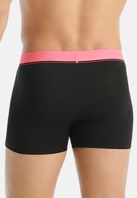 Svarta badshorts med en strukturerad rosa midjeband och kontrasterande sömmar. Materialet verkar slätt och formar sig efter kroppen.