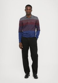 Polo de manga longa com riscas horizontais em vermelho, azul e cinza. Calças pretas e sapatos pretos completam o look.