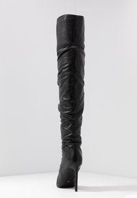 Schwarze Lederstiefel über dem Knie mit einem lässigen Design, hohem Stiletto-Absatz und glatter Textur. Verfügt über genähte Einsätze für zusätzliche Details.