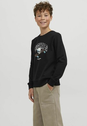 Felpa nera con grafica di teschio e skateboard. Polsini e bordo a coste, indossata con pantaloni cargo beige. Texture liscia, design casual.