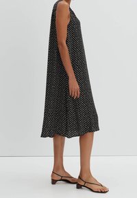 Musta, hihaton mekko, jossa on valkoisia pilkkuja; täysin A-linjainen siluetti ja polveen saakka ulottuva helma. Yhdistetty yksinkertaisiin mustiin sandaaleihin.