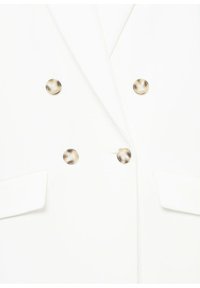 Blazer blanc à double boutonnage avec quatre boutons ronds dorés et deux poches à rabat à l'avant.