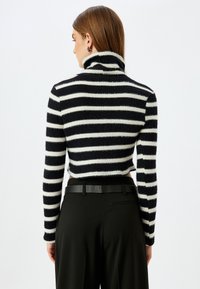 Gestreifter Rollkragenpullover in Schwarz und Weiß, flauschige Textur, taillierte Passform, lange Ärmel, kombiniert mit hoch taillierten schwarzen Hosen und Gürtel.