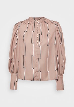 Blouse beige à manches longues avec col montant, rayures géométriques verticales noires et blanches, et une rangée de petits boutons à l'avant.