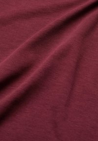 Burgundské bavlněné tkaniny s hladkým povrchem, na kterém se ukazují jemné natažení a záhyby. Rovnoměrná barva s minimálním vzorem, vhodná pro oděvy nebo čalounění.