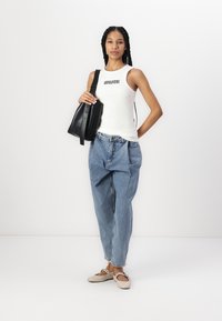 Hvid tanktop med "MUSH" tekst, parret med løse blå denimjeans og beige slip-on sko. Sort håndtaske med en kort rem.