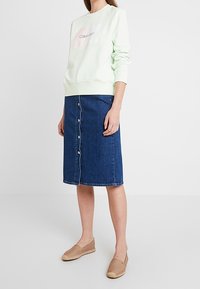 Světlá mátová mikina s logem "Calvin Klein", kombinovaná s modrou džínovou sukní po kolena se zapínáním na knoflíky vpředu a béžovými espadrilkami na došlápnutí.