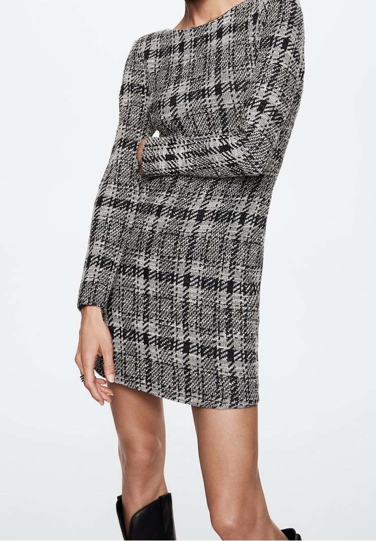 Femme portant une mini-robe à manches longues pied-de-poule noir et blanc, bras croisés et bottes noires sur fond blanc.