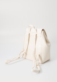 Witte leren rugzak met een trekkoordsluiting, platte bandjes en een gestructureerde vorm. Bevat minimale hardware en heeft een gladde textuur.