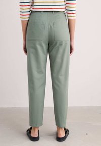 Pantalons en coton vert clair au design droit, avec deux poches arrière et une coupe cropped, associés à des sandales plates noires.