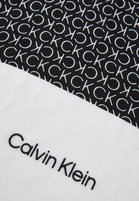 Black and white fabric featuring repeating "CK" logo pattern. Smooth texture with a prominent "Calvin Klein" label in black on a white section.
