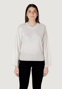 Maglione V-neck crema con maniche lunghe, caratterizzato da un motivo a diamante testurizzato e polsini e orlo a coste. Abbinato a pantaloni neri.