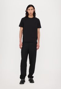 Svart crew neck t-skjorte i kombinasjon med svarte løse bukser og svarte sko; minimalistisk design, glatt tekstur, ingen synlige logoer.