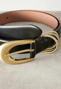 Svart läderbälte med en stor gul oval spänne, med tre extra gul- och silverringar för justering, slät yta.