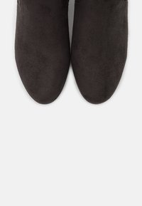 Stivali alla caviglia neri in suede, con una superficie liscia, punta tonda, cuciture minime e senza hardware o accenti visibili.