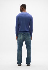 Blauer Pullover mit rundem Ausschnitt, kombiniert mit verblassten blauen Jeans im Straight-Leg-Stil. Das Outfit zeichnet sich durch sichtbare Nähte und zwei Gesäßtaschen aus.