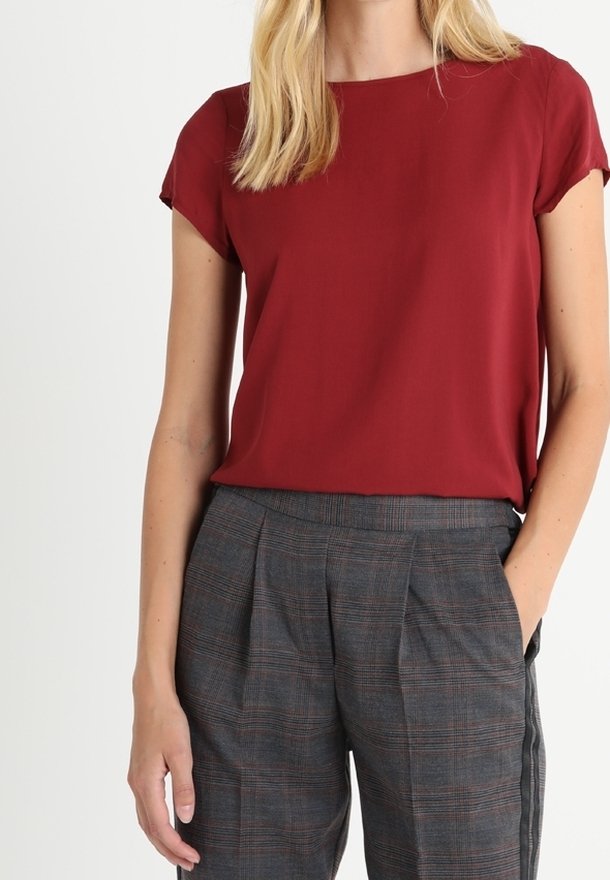 Blusa corta de manga corta color marrón con cuello redondo, combinada con pantalones de cuadros grises de corte relajado y bolsillos laterales.