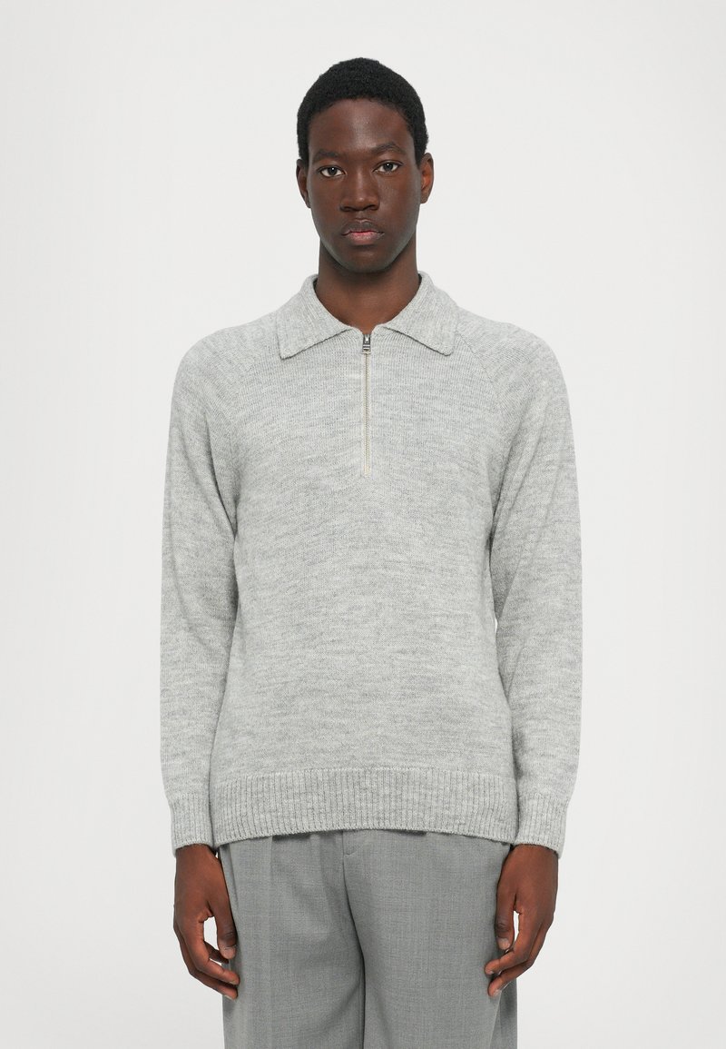 Jersey gris con medio cierre y cuello de punta; presenta puños y dobladillo acanalados. Se lleva con pantalones gris claro.