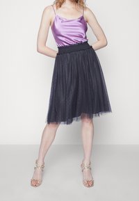 Camisole in raso viola con spalline sottili abbinata a una gonna in tulle nera al ginocchio con vita arricciata e sottili accenti glitterati.