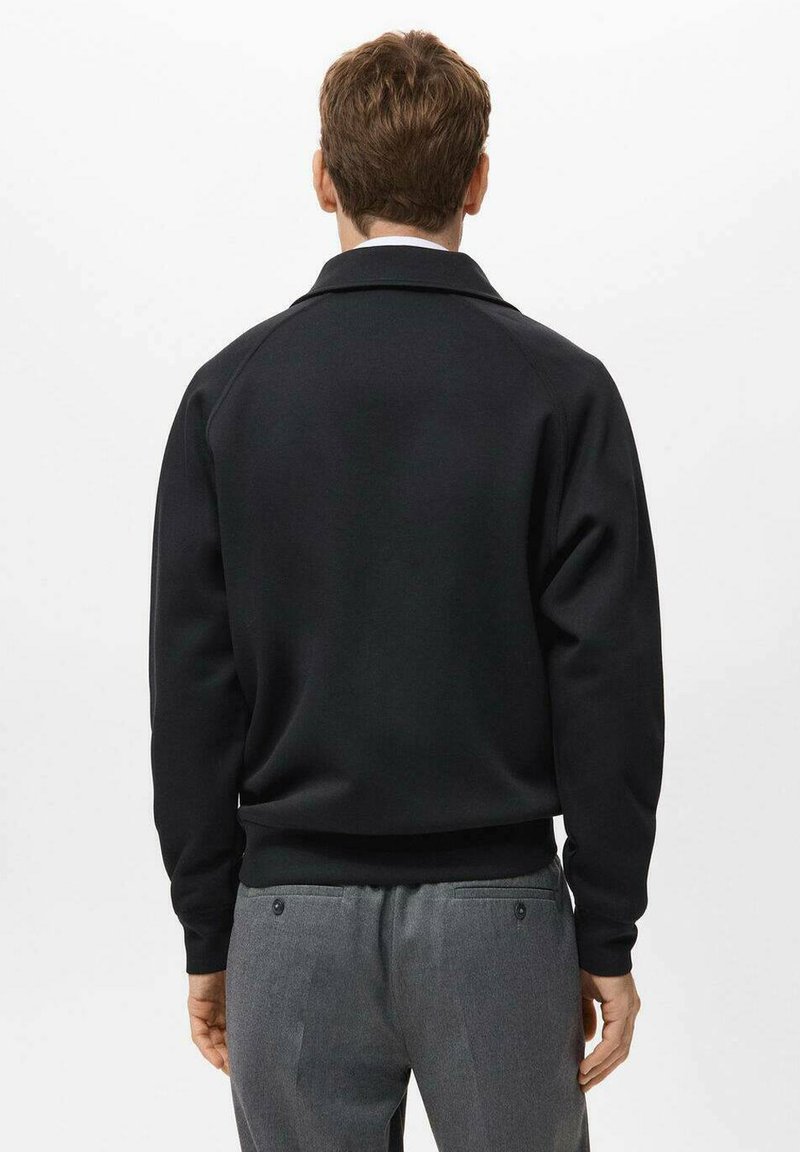 Schwarzer Sweatshirt mit einfacher Gestaltung, gerippten Bündchen und Saum. Verfügt über einen klassischen Kragen. Getragen mit grauen Hosen. Hinteransicht.