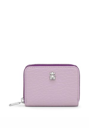 Una pequeña cartera color lavanda con cremallera perimetral y acabado texturizado, cremallera morada, cierre plateado y un emblema de osito está sobre un fondo blanco.