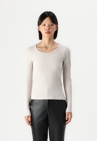 Light beige long-sleeve top with a ribbed texture and a rounded neckline, paired with black leather pants. Simple, fitted design.