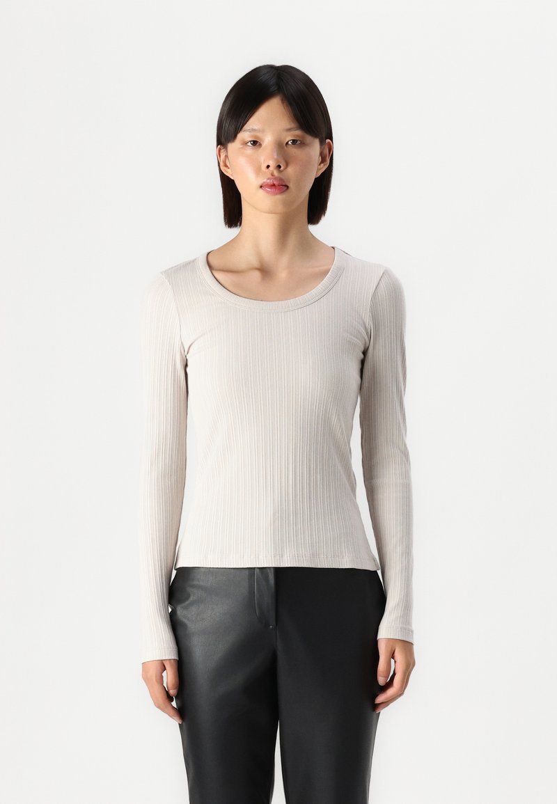 Light beige long-sleeve top with a ribbed texture and a rounded neckline, paired with black leather pants. Simple, fitted design.
