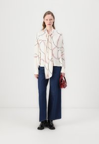 Camicia bianca con motivo a catena rosso e nero, dettaglio con nodo al collo; jeans a gamba larga blu; stivaletti neri; piccola borsa rossa.