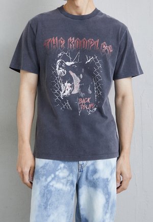 Schwarzes Baumwoll-T-Shirt mit einem Grafikdesign eines bellenden Hundes vor einem Maschendraht-Hintergrund, mit "THE KOOPLES" und "BACK TO LIFE" in roten Buchstaben.