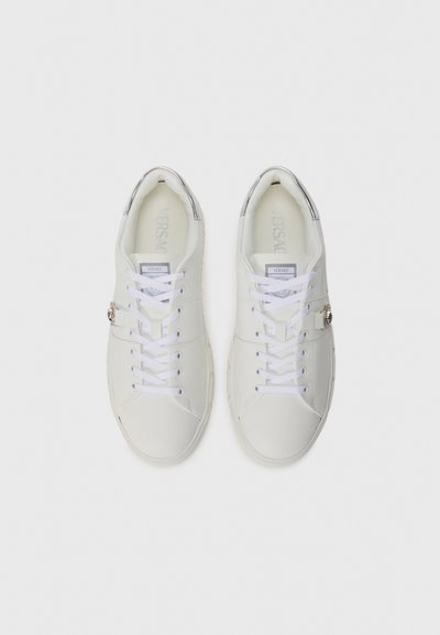 White leather sneakers with round toes, white laces, and metallic accents on the heel. Features a subtle logo on the tongue.