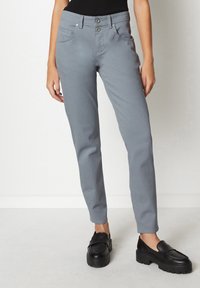 Pantalones de mezclilla gris de corte slim, con una cintura alta, dos bolsillos delanteros y cierre de botón. Llevados con zapatos de plataforma negros.