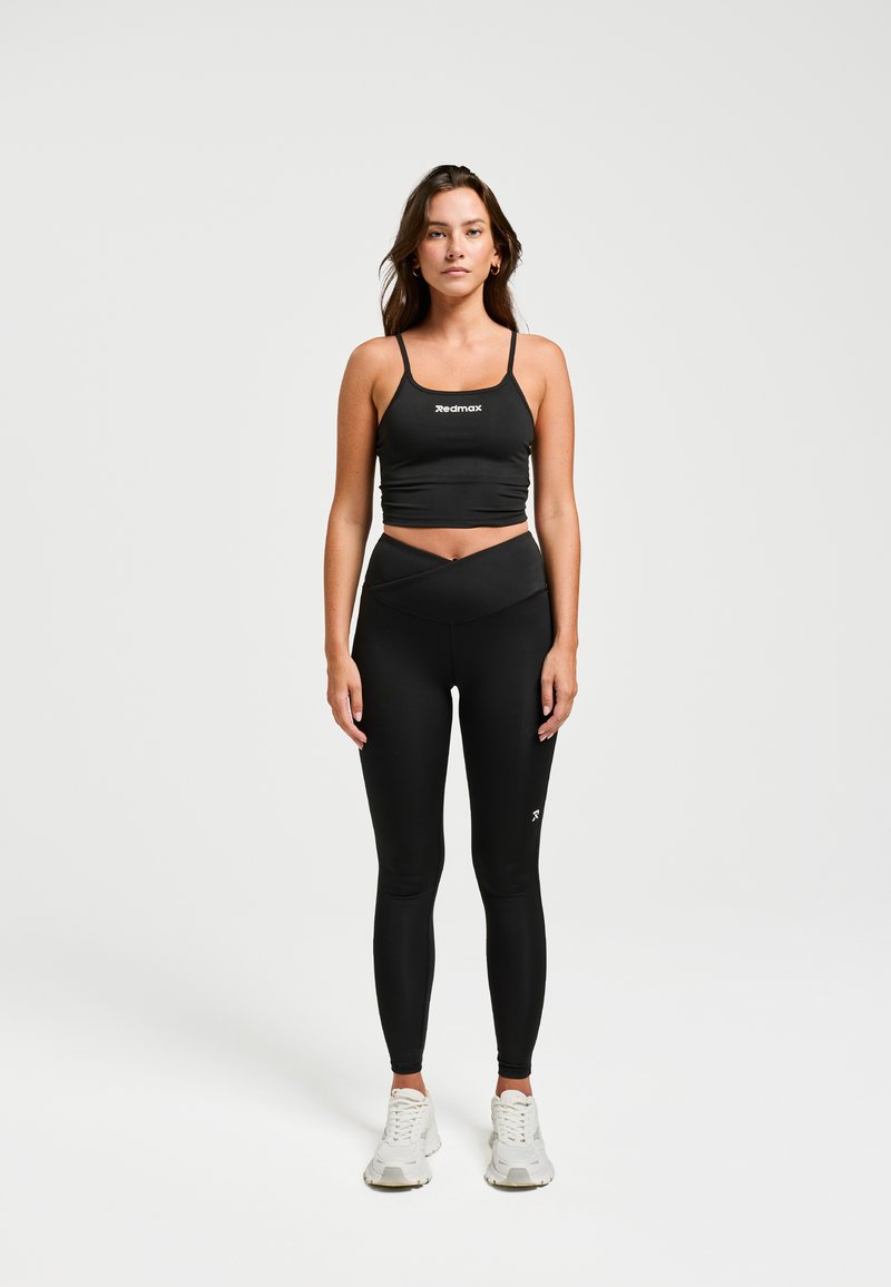 Zwarte sportbeha met dunne banden en logo. Gemaakt in combinatie met hoog-getailleerde zwarte leggings met een crossover-ontwerp. Grijze sneakers.