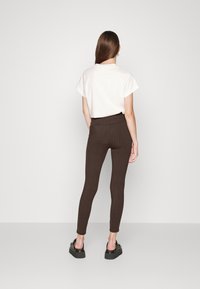 Leggings marrones con estampado y cintura alta, hechos de un material elástico. Combinados con una camiseta blanca holgada y zapatos de plataforma negros.