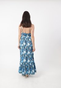 Robe maxi avec un motif floral bleu, des bretelles spaghetti, un corsage smocké et un ourlet évasé. Fabriquée en tissu léger avec une coupe fluide.
