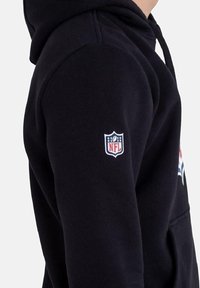 Felpa nera con cappuccio, dotata di una patch con il logo NFL sul maniche sinistro e una tasca a marsupio sulla parte frontale. Materiale in cotone morbido.