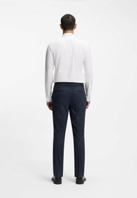 Witte overhemd met lange mouwen en donkerblauwe broek gezien vanuit de achterkant, met een getailleerde pasvorm, een gladde textuur en een subtiele glans.