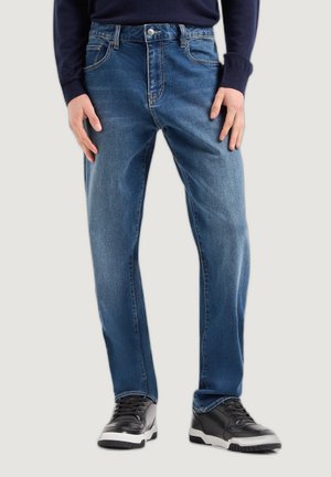 Jeans in denim azzurro chiaro con vestibilità dritta, cinque tasche, cuciture rinforzate e chiusura con bottone. Indossati con sneakers nere.