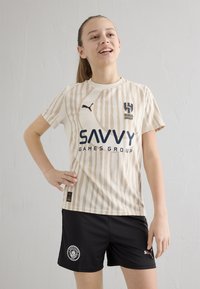 Ljusbeige randig sporttröja med mörkblå "SAVVY"-logotyp och lagemblem, tillsammans med svarta shorts med en cirkulär logotyp. Lättviktigt tyg.
