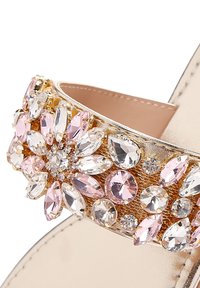 Cinturino dorato per sandali decorato con pietre di rhinestone rosa e trasparenti di varie forme. Finitura liscia e metallica con un arrangiamento floreale degli abbellimenti.