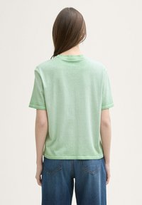 T-shirt en coton vert clair à manches courtes avec une coupe décontractée et un col rond, montré de dos, associé à un jean en denim bleu.