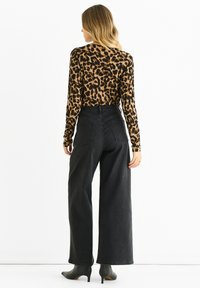 Top a maniche lunghe con stampa leopardata abbinato a jeans neri a vita alta e ampio. Il tessuto ha una consistenza liscia.
