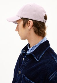 Helle lila Baseballmütze aus Baumwolle mit verstellbarem Riemen auf der Rückseite. Getragen mit einer marineblauen Cordjacke und einem blauen gestreiften Hemd.