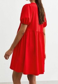 Robe rouge texturée avec manches bouffantes et jupe évasée, dotée d'un tissu tissé lisse et d'un design à hauteur de genoux.