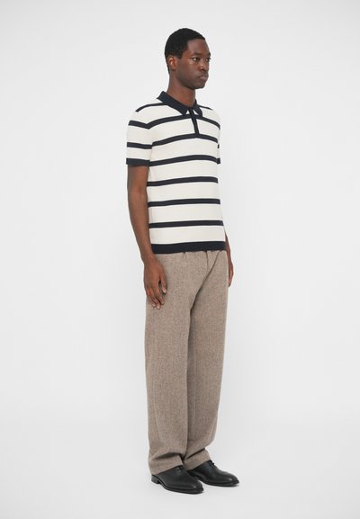 Csíkozott póló ing krém és sötét tengerész kék színben, gallérral. Világosbarna, laza szabású nadrággal párosítva. Fekete cipők egészítik ki az öltözetet.