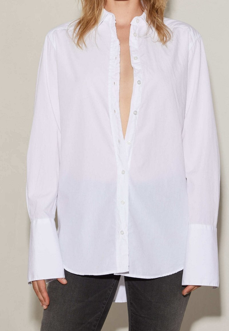 Chemise blanche à boutons avec des manches longues et un décolleté en V profond, dotée d'une patte froncée et de larges poignets, fabriquée dans un tissu léger.