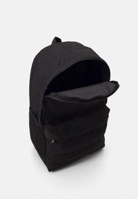 Mochila preta com um compartimento principal com fecho, uma aba plana e bolsos laterais em malha. Tecido texturizado com um acabamento suave e design minimalista.