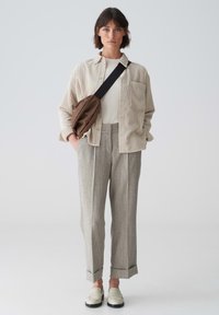 Light beige striped shirt, white top, patterned gray trousers with cuffs, and cream loafers. Brown sling bag adds contrast to outfit.