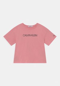 Camiseta de algodón rosa con mangas cortas, cuello redondo y un logo negro de "CALVIN KLEIN" impreso en el frente. Diseño sencillo y holgado.